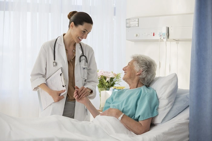 Médica atende paciente idosa que está deitada em uma cama. Falando sobre como solicitar procedimento para a sulamérica saúde.