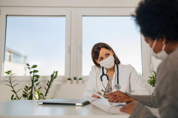 Médica conversa com paciente. Ela está com uma máscara e um estetoscópio. Explicando como cadastrar no sulamérica saúde boaconsulta.