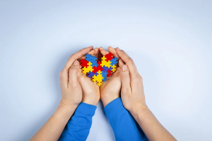 Adulto envolve as mãos de criança que segura símbolo do espectro autista. Falando sobre o melhor plano de saúde para autismo.