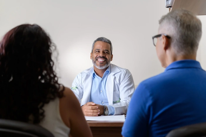Médico sorridente conversa com casal de pacientes. Explicando se câncer curado é doença preexistente.