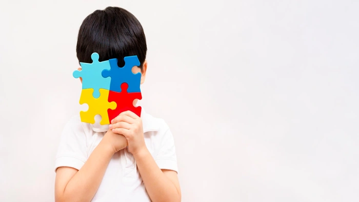 Criança segura símbolo do espectro autista na frente do rosto. Falando sobre o melhor plano de saúde para autismo.
