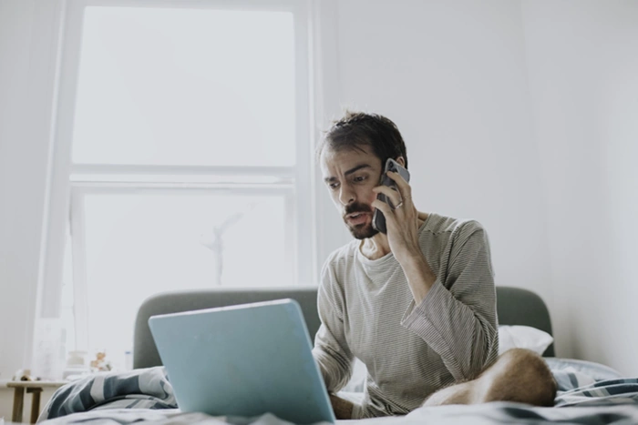 Homem reclama ao telefone ao consultar algo em um notebook. Falando sobre onde reclamar de plano de saúde.