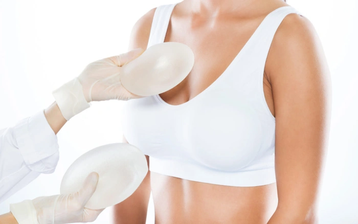 Médico aproxima duas próteses aos seios de uma paciente. Falando sobre "plano de saúde cobre silicone?".